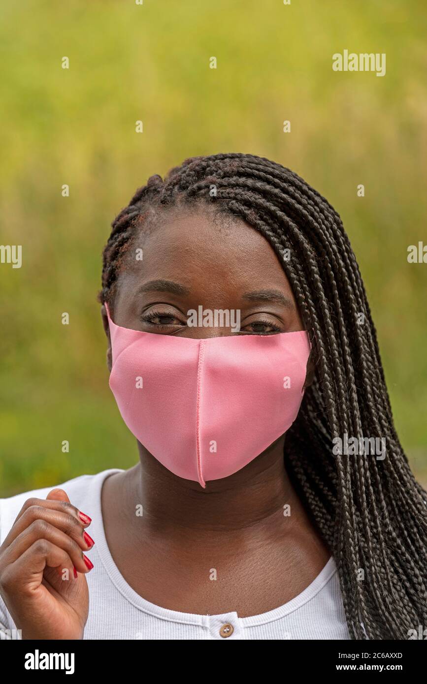 Angleterre, Royaume-Uni. 2020. Portrait d'une femme noire avec un style de cheveux tressé et portant un masque rose pendant l'épidémie de Covid-19 Banque D'Images