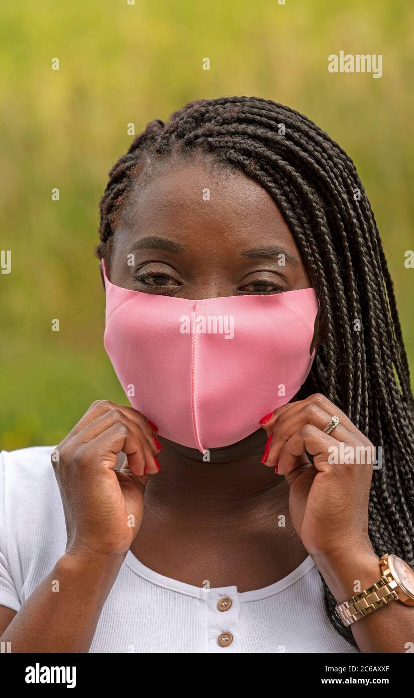 Angleterre, Royaume-Uni. 2020. Portrait d'une femme noire avec un style de cheveux tressé et portant un masque rose pendant l'épidémie de Covid-19 Banque D'Images