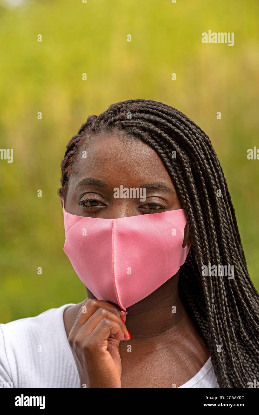 Angleterre, Royaume-Uni. 2020. Portrait d'une femme noire avec un style de cheveux tressé et portant un masque rose pendant l'épidémie de Covid-19 Banque D'Images