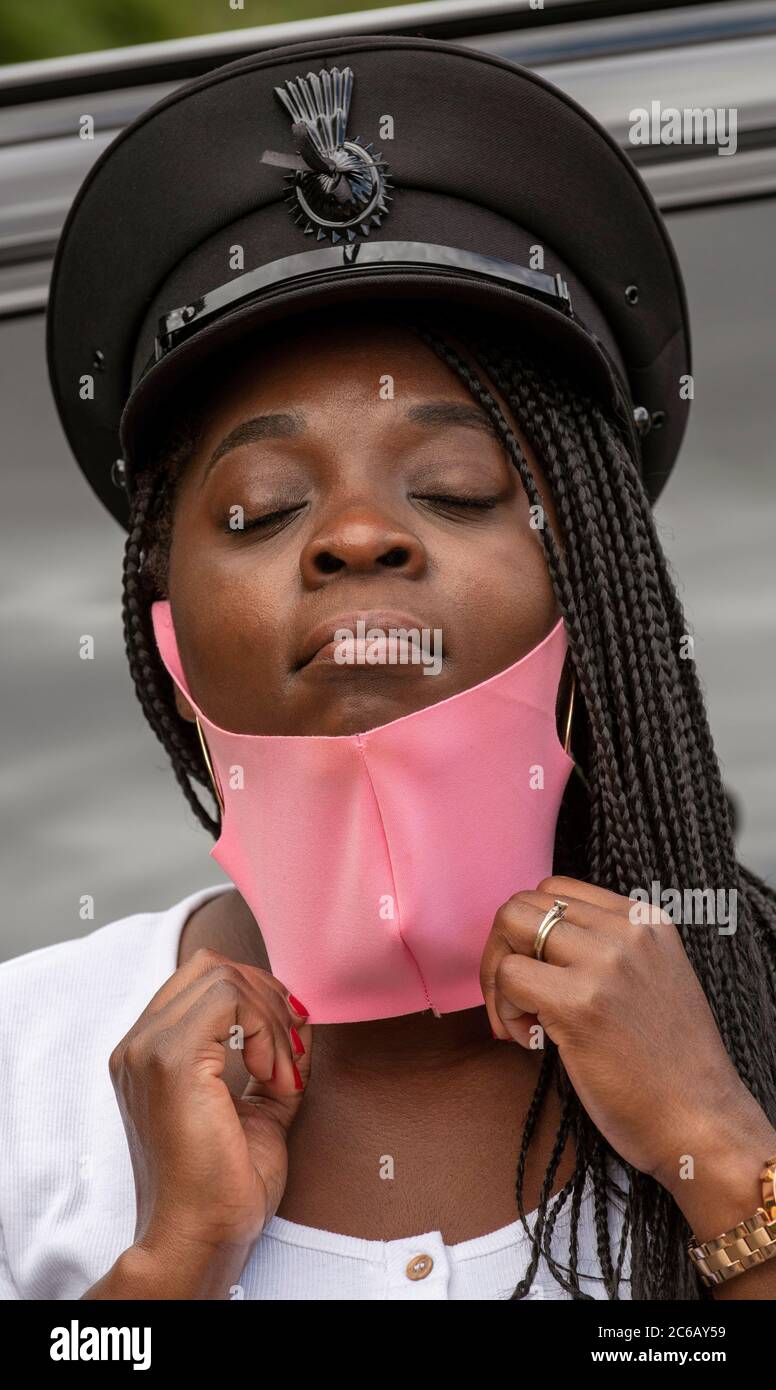 Angleterre, Royaume-Uni. 2020. Portrait d'une femme chauffeur avec une  casquette uniforme et des cheveux tressés ajustant son masque rose pendant  l'épidémie de Covid-19 Photo Stock - Alamy