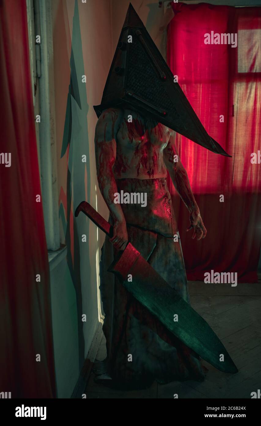 Cosplayer à l'image du bourreau se tient dans une pièce sombre avec un couteau dans la main et un casque sur la tête. Banque D'Images