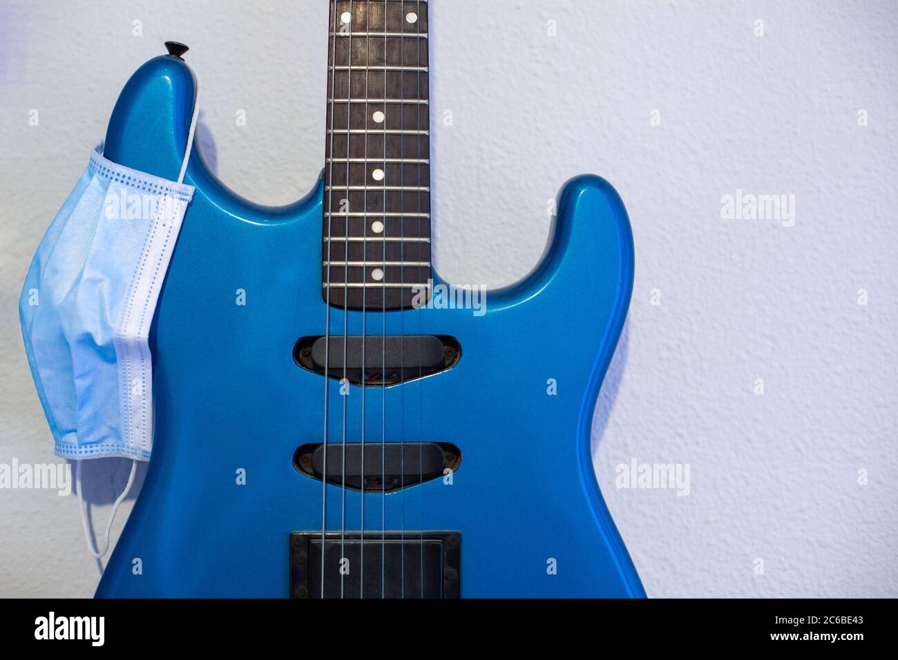 Concept d'isolement : guitare électrique bleue fixée au mur avec un masque sanitaire. Banque D'Images