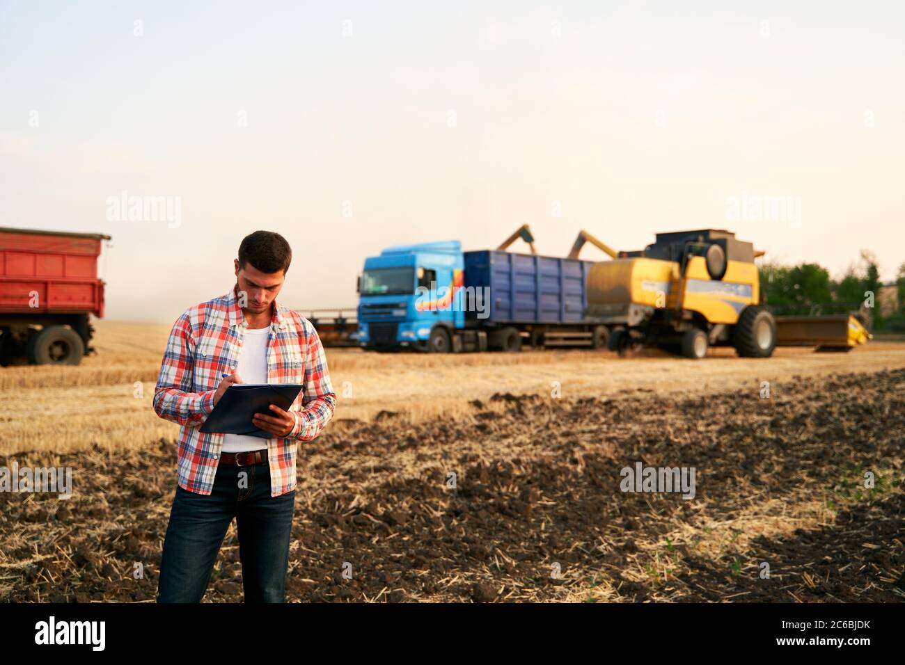 L'agriculteur commande le chargement du blé de la récolteuse au camion à grains. Le conducteur tient le presse-papiers, garde les notes, compte de la cargaison. Le transitaire remplit l'envoi Banque D'Images