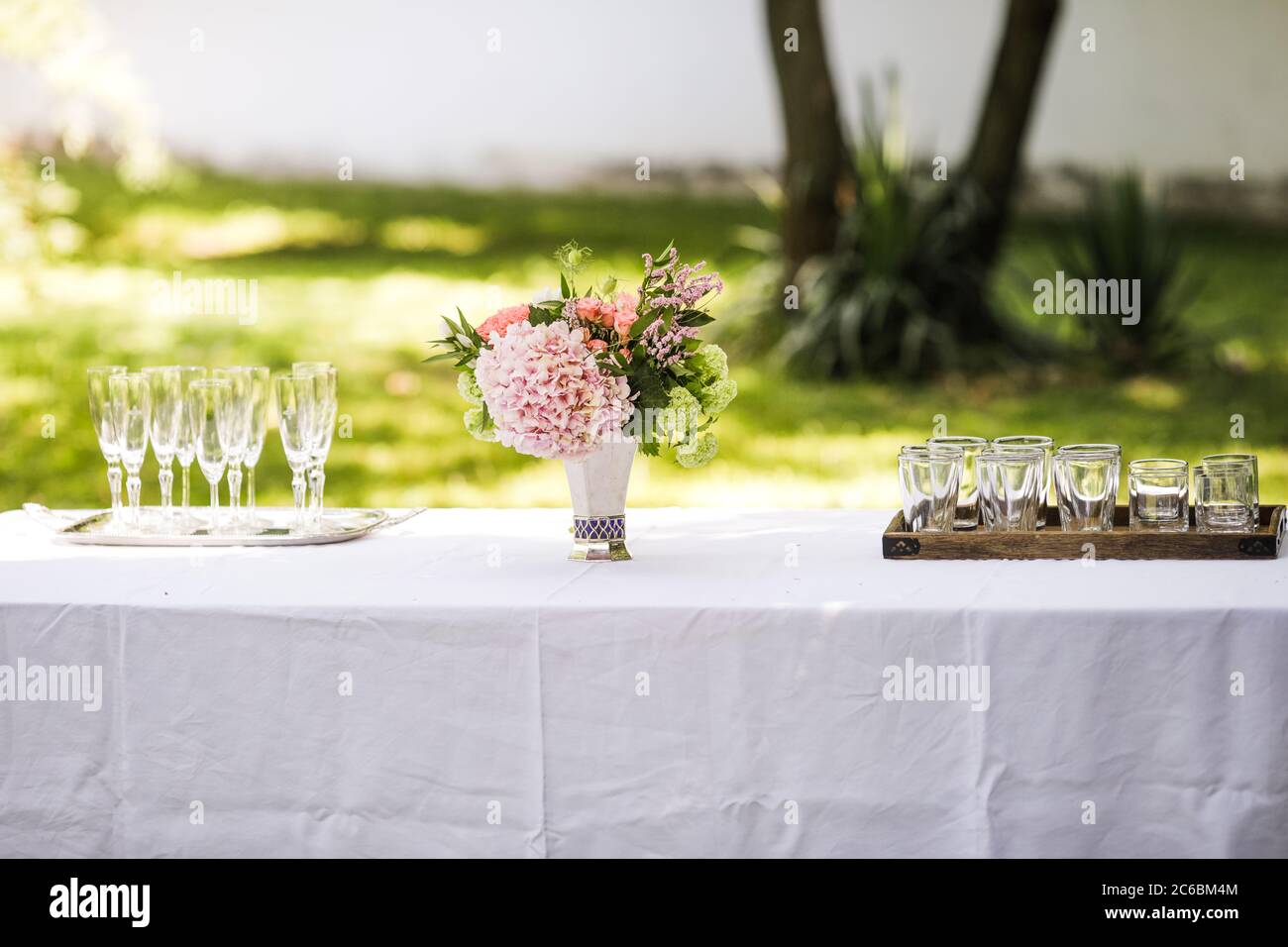 Bouquet de fleurs et verres vides sur une table dans un jardin pendant une journée d'été avant un toast. Banque D'Images