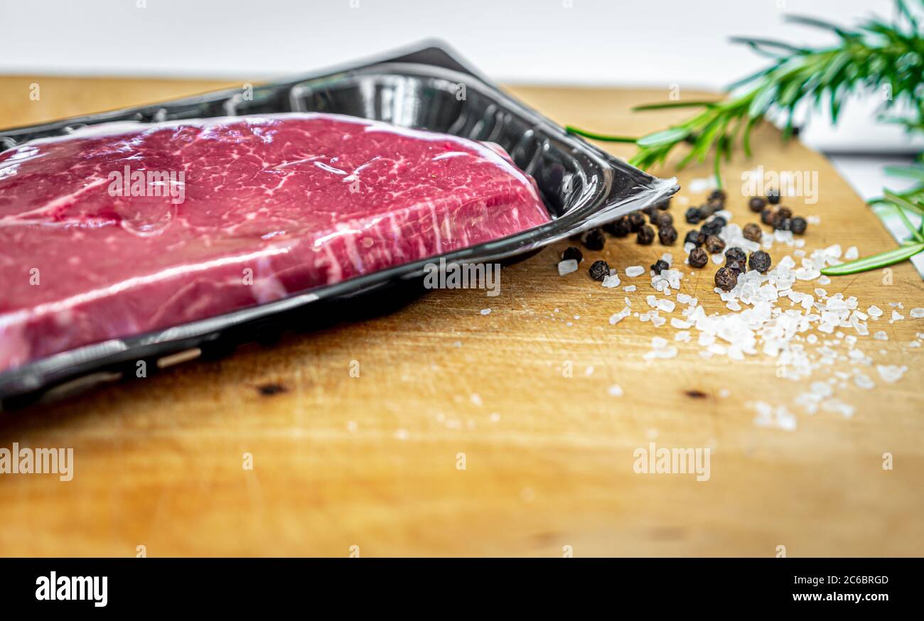 Steak de bœuf dans un emballage sous vide et épices sur planche à découper en bois avec espace d'imitation Banque D'Images