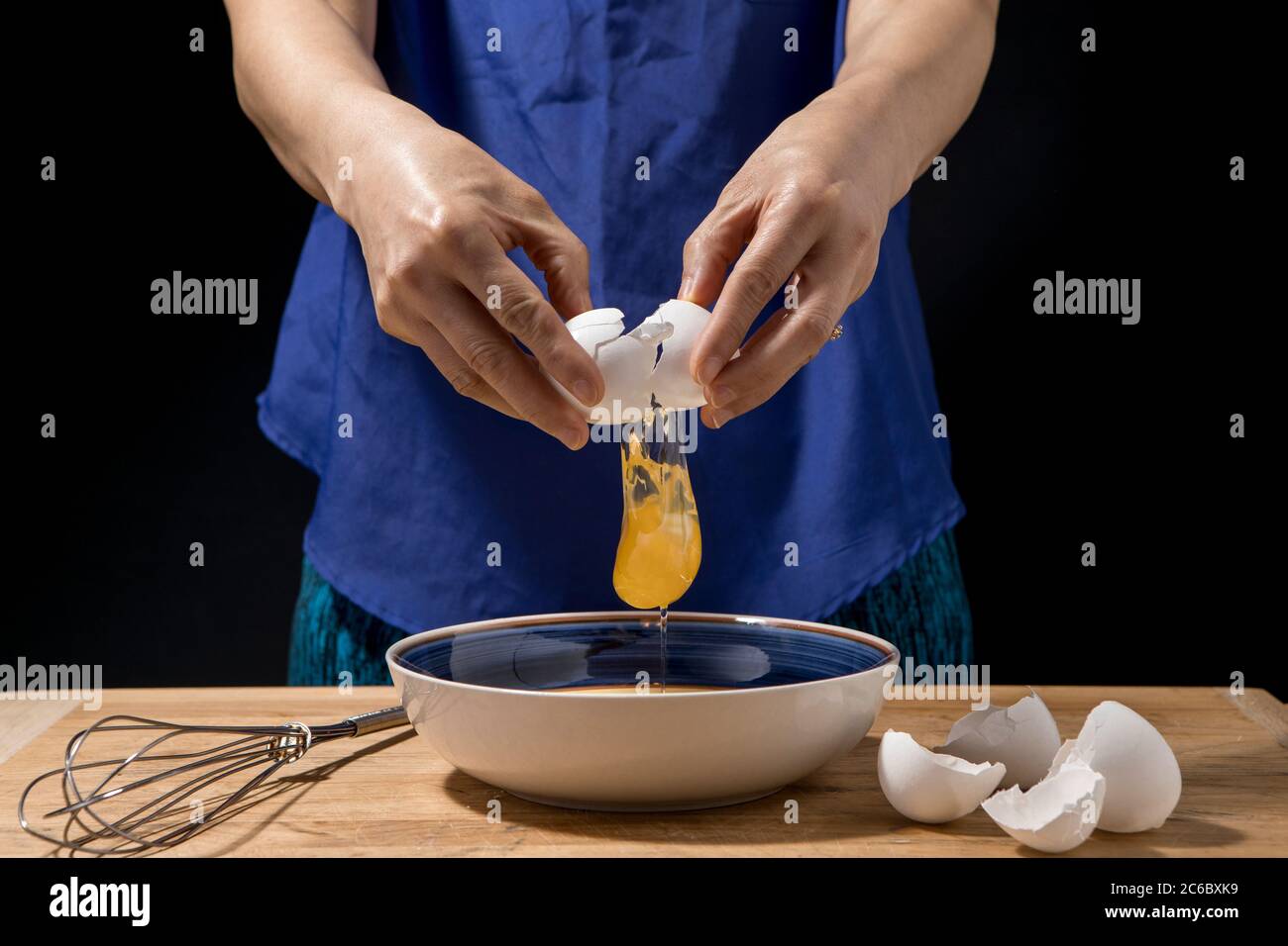 Une femme se fend et l'oeuf et le jaune tombe au bol. Banque D'Images