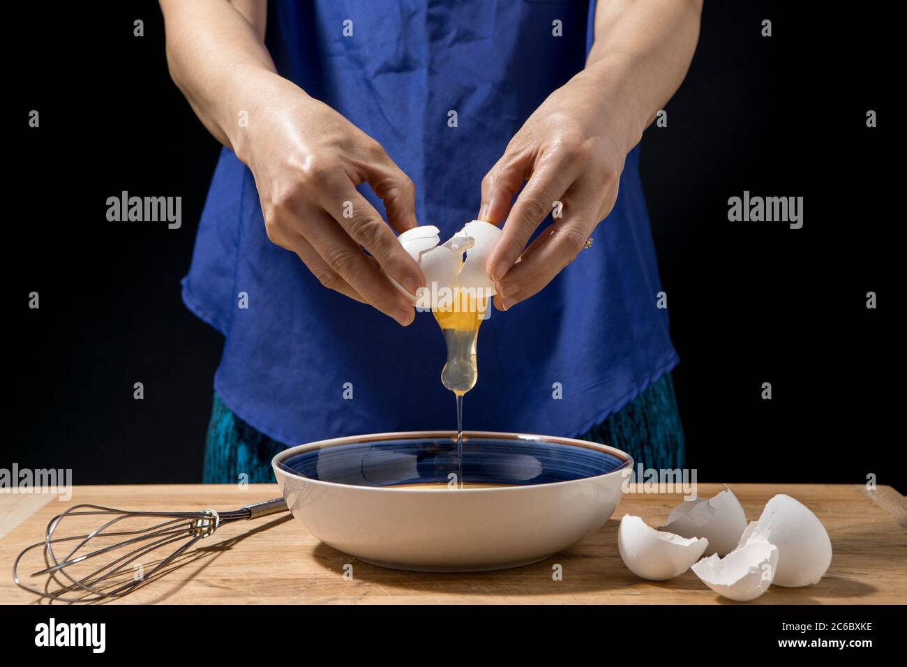 Une femme se fend et l'oeuf et le jaune tombe au bol. Banque D'Images