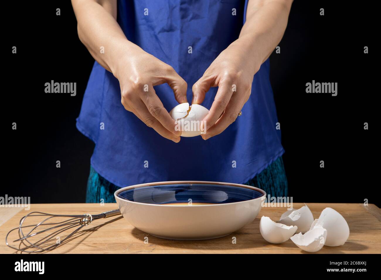 La femme fend un œuf pour le mettre dans un bol à mélanger. Banque D'Images