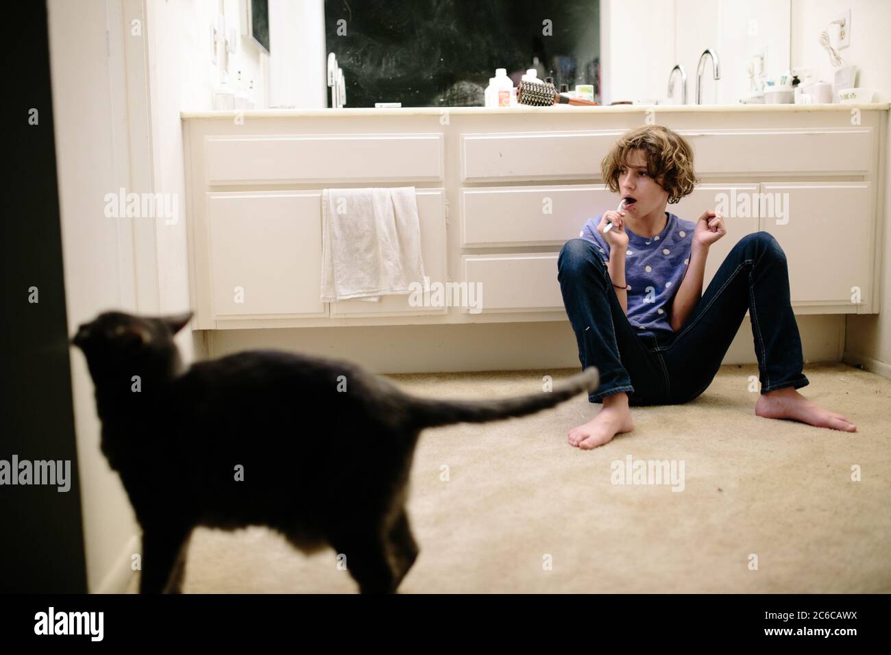Une jeune fille est assise sur le sol tout en se brossant les dents avec cat à proximité Banque D'Images