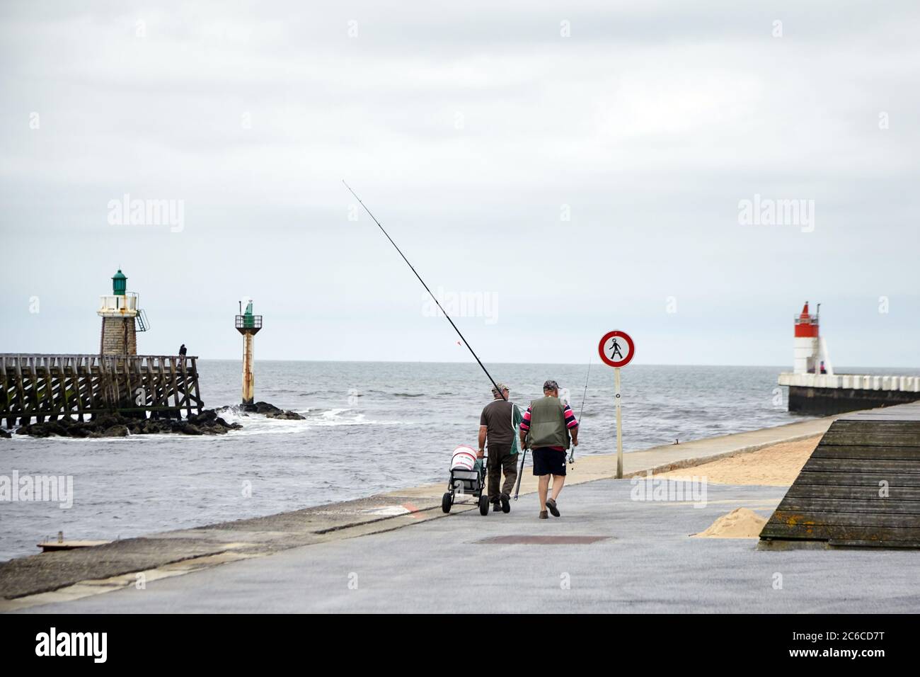 Capbreton, France - 19 juin 2018 : pêcheurs marchant le long de la jetée avec des cannes à pêche et une voiturette sur le fond de l'océan Atlantique et de la lumière Banque D'Images