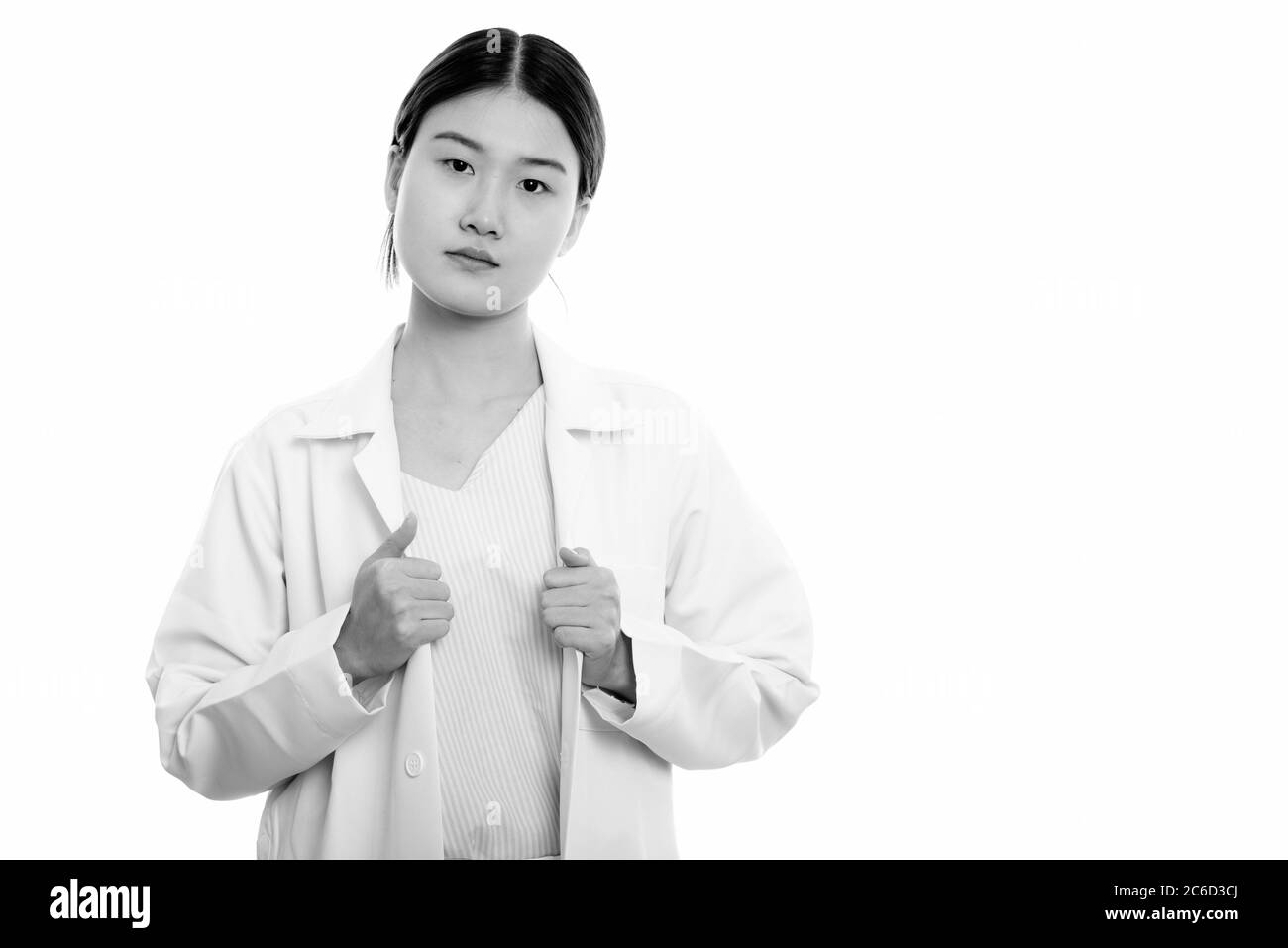 Photo de studio de jeune femme asiatique belle médecin tenant un manteau de laboratoire avec les deux mains Banque D'Images