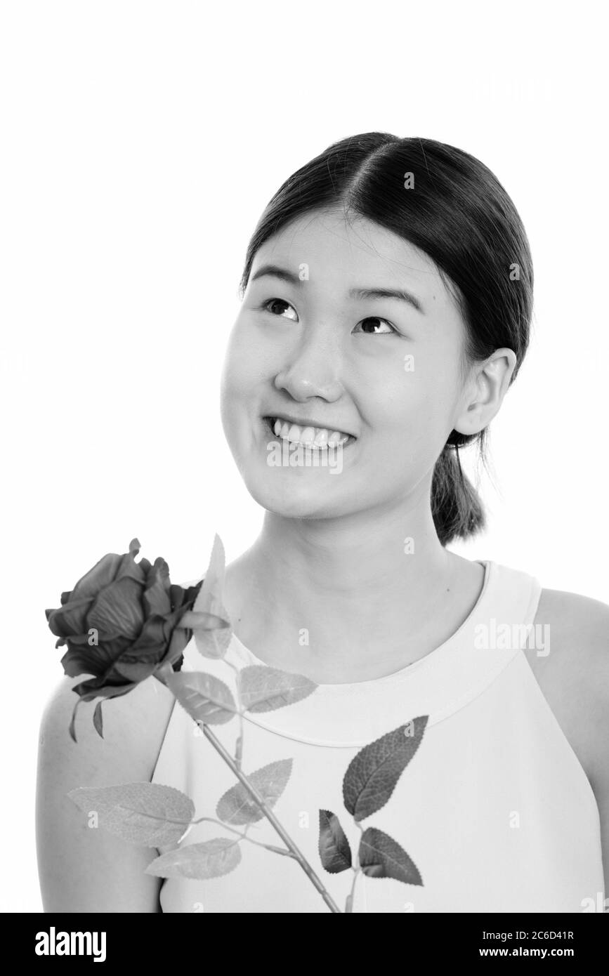 Photo studio d'une jeune femme asiatique heureuse souriant et tenant la rose rouge tout en pensant Banque D'Images