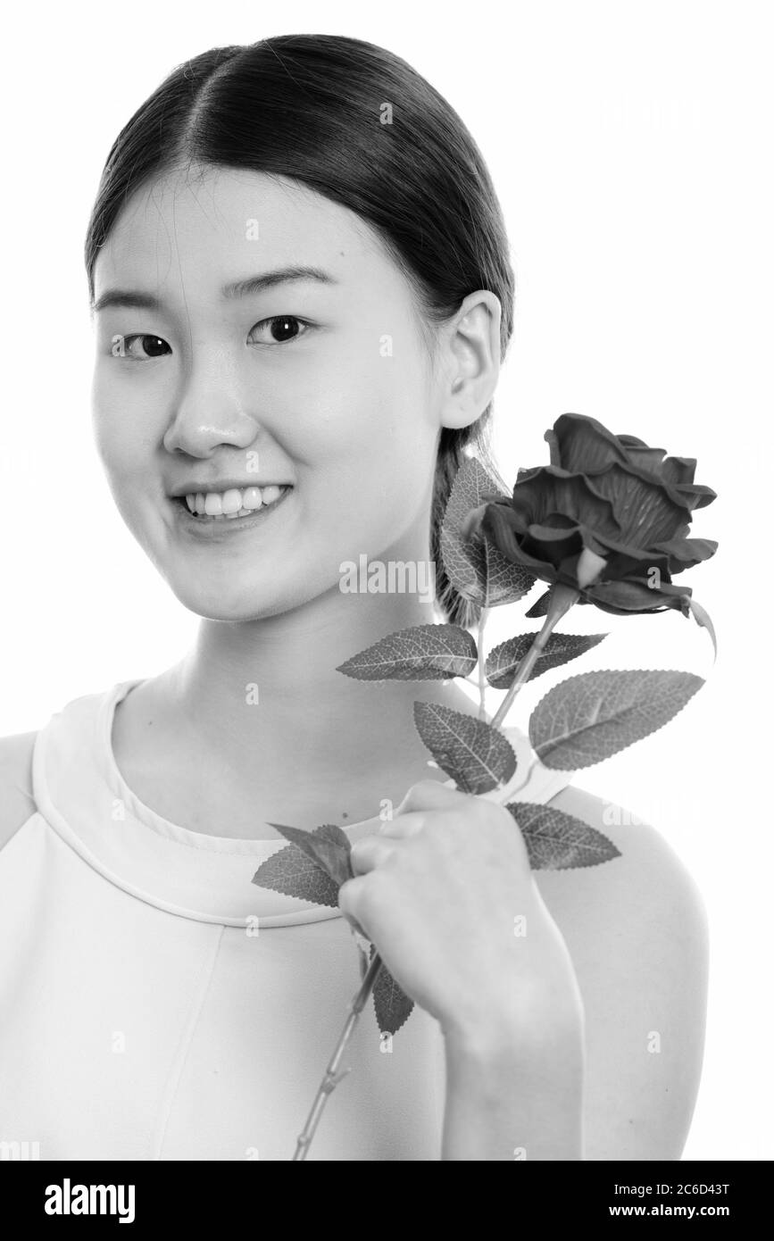 Gros plan de la jeune femme asiatique heureuse souriant et tenant la rose rouge près du visage Banque D'Images