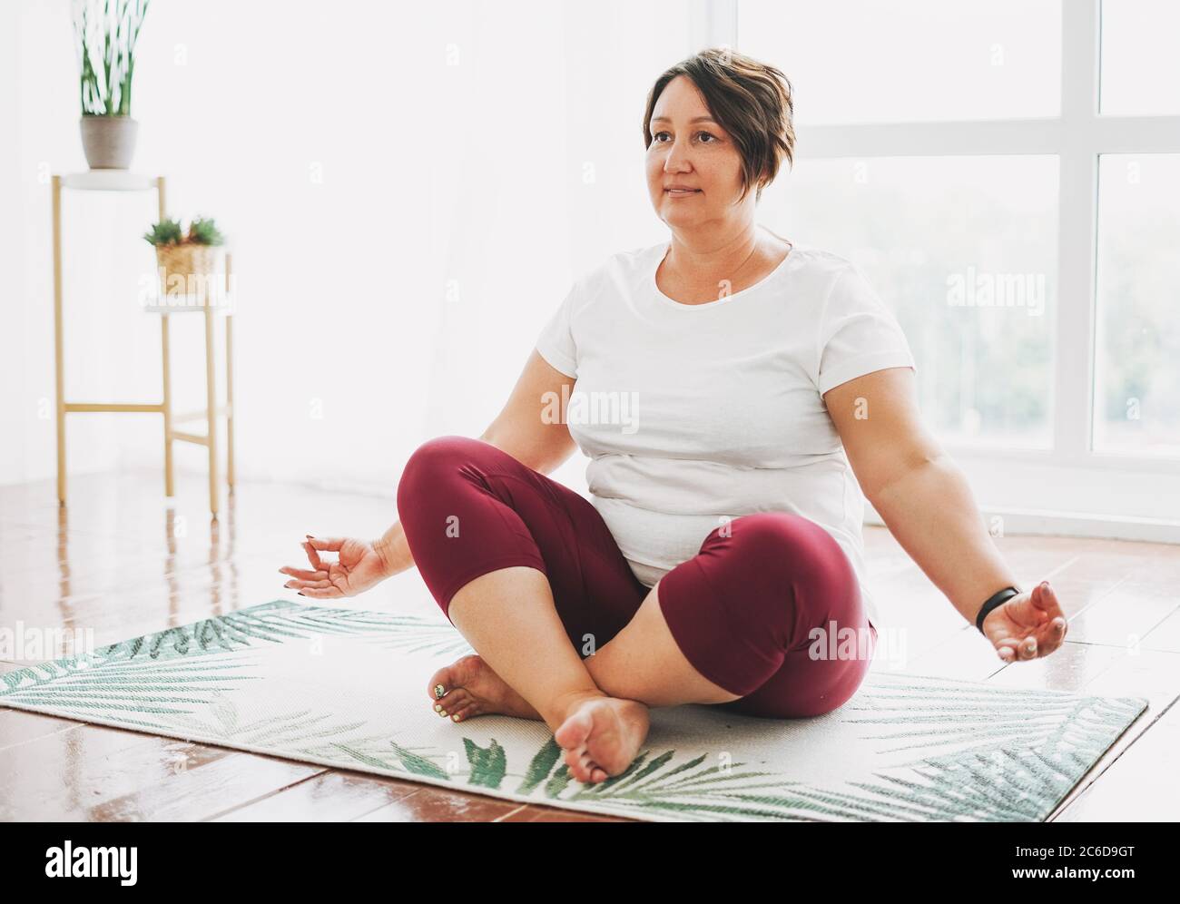 Femme brune charmante adulte plus la taille corps pratique positive yoga dans un studio lumineux Banque D'Images