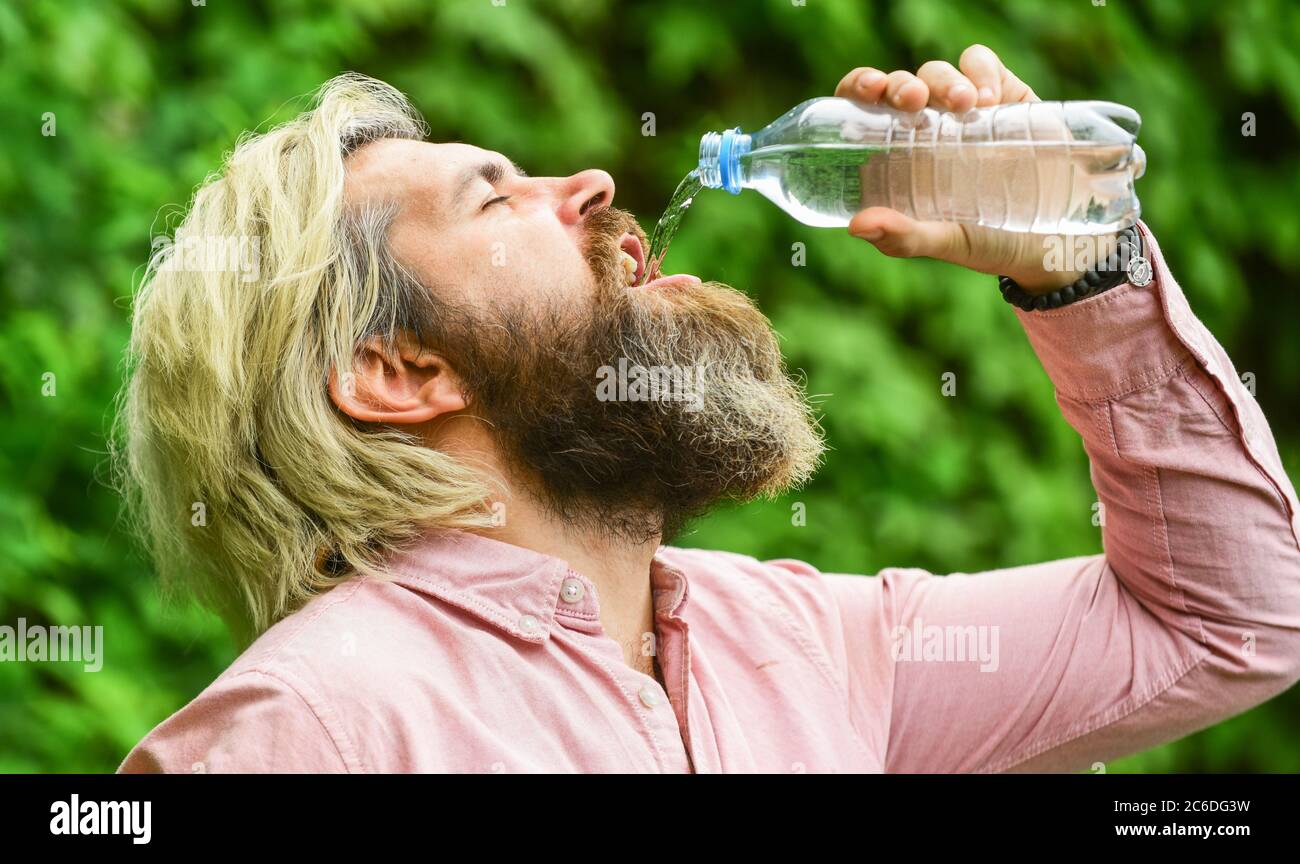 Équilibre de l'eau. Homme barbu touriste eau potable bouteille plastique nature fond. Un gars assoiffé qui boit de l'eau en bouteille Un mode de vie sain. Sécurité et santé. Chaleur estivale. Boire de l'eau claire. Banque D'Images
