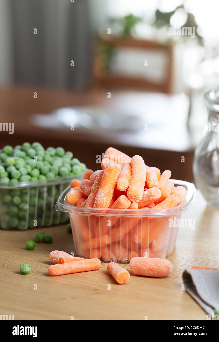 Les légumes surgelés comme les carottes et les petits pois dans les boîtes  de rangement sur la table de cuisine. La congélation est une méthode sûre  pour augmenter la durée de conservation
