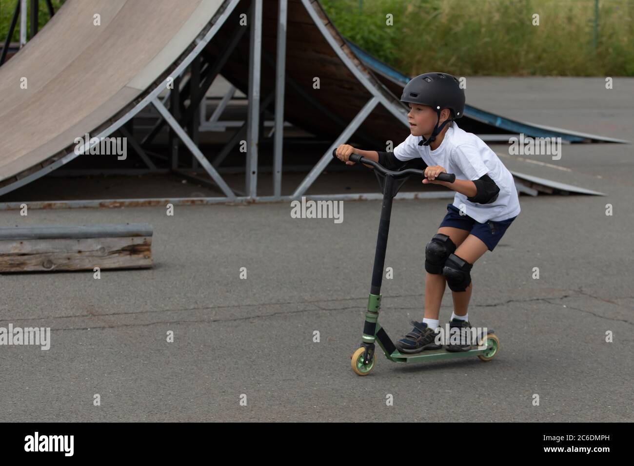 Un petit garçon mignon fait un scooter dans un parc à roulettes. Un jeune athlète novice passe du temps libre dans les sports extrêmes. Style de vie. Banque D'Images