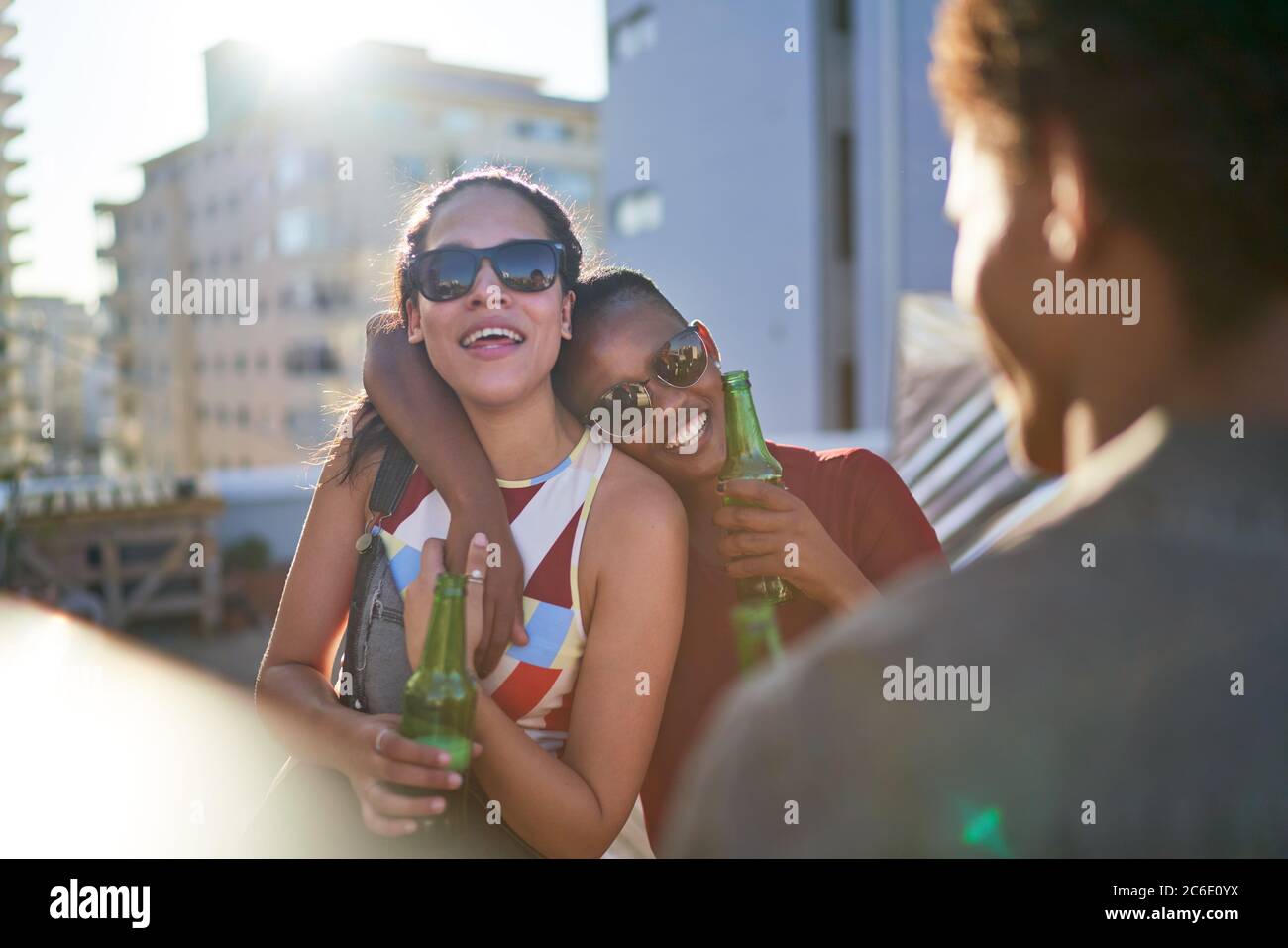 De jeunes amies joyeuses boivent de la bière sur le toit ensoleillé de l'été Banque D'Images