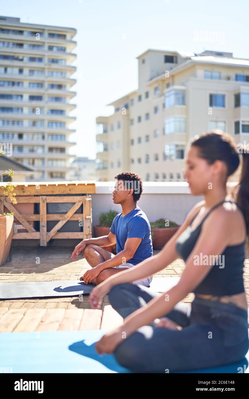 Jeune homme et femme pratiquant le yoga sur un toit urbain ensoleillé Banque D'Images Jeune homme et femme pratiquant le yoga sur un toit urbain ensoleillé Banque D'Images