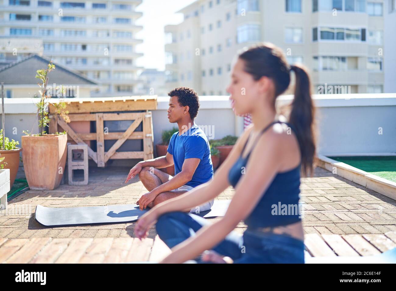Jeune homme et femme pratiquant le yoga sur un toit urbain ensoleillé Banque D'Images Jeune homme et femme pratiquant le yoga sur un toit urbain ensoleillé Banque D'Images