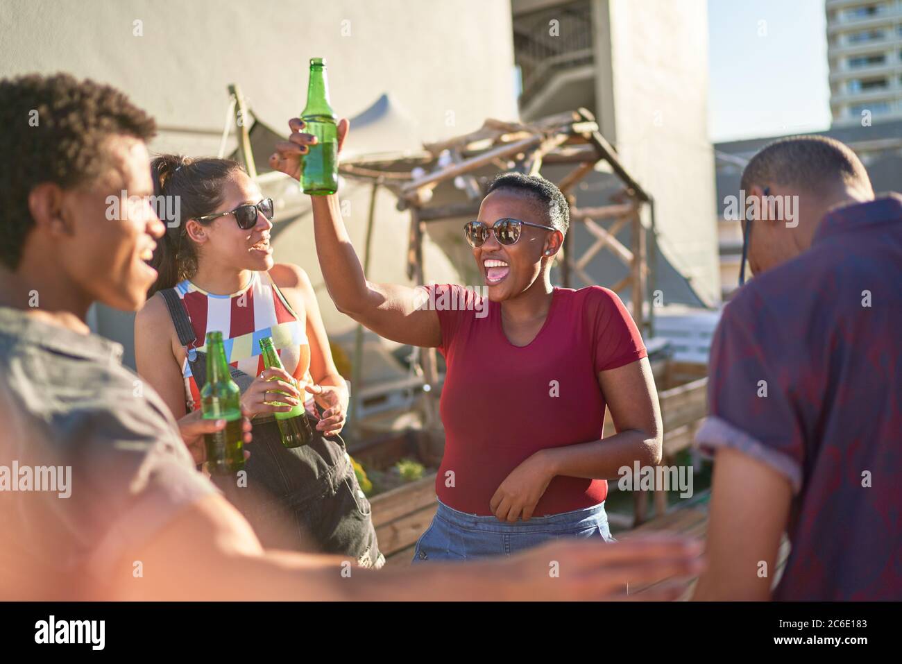 De jeunes amis heureux dansant et buvant de la bière sur un balcon ensoleillé Banque D'Images