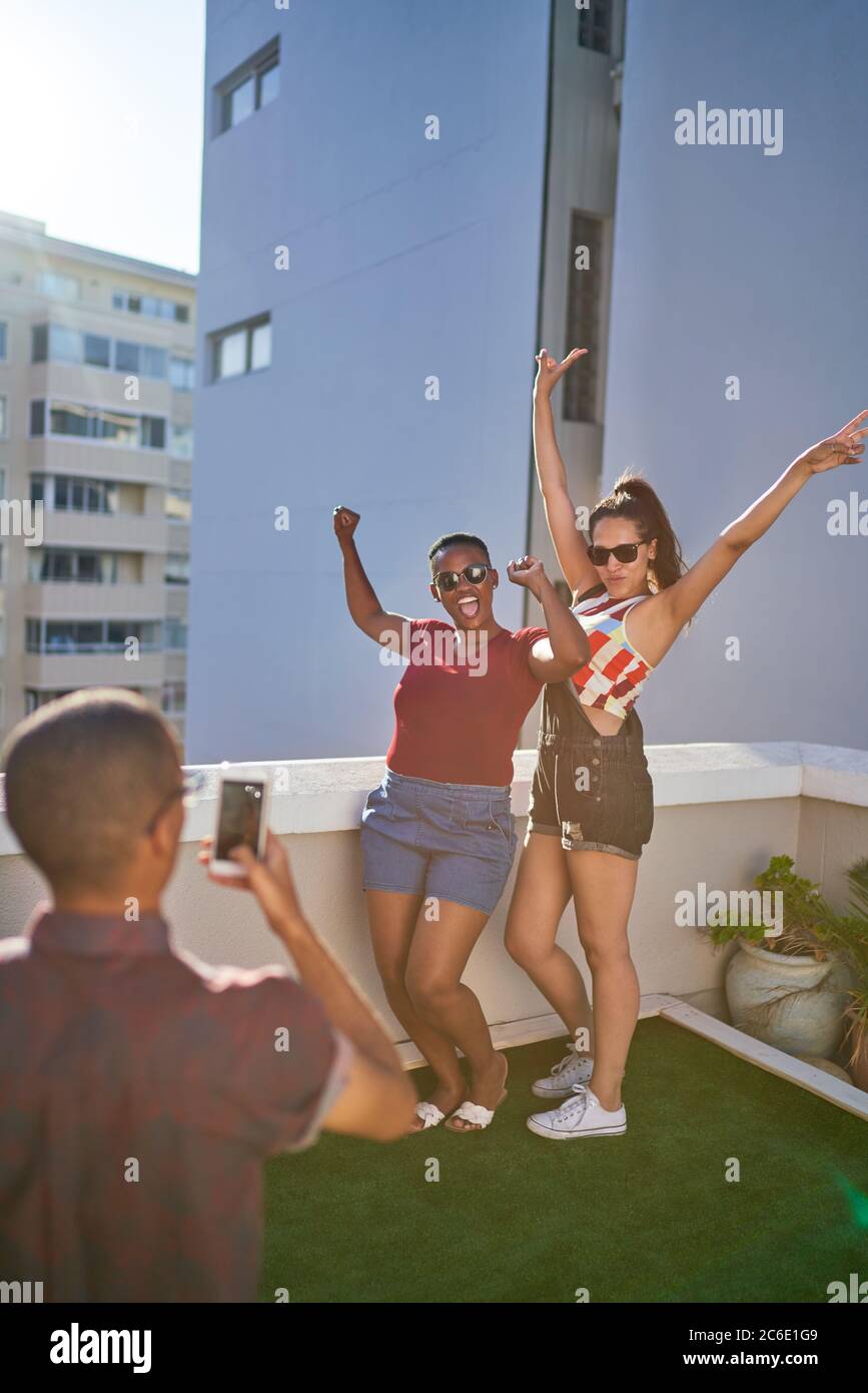 De jeunes amies joyeuses posant pour la photo sur un balcon urbain ensoleillé Banque D'Images