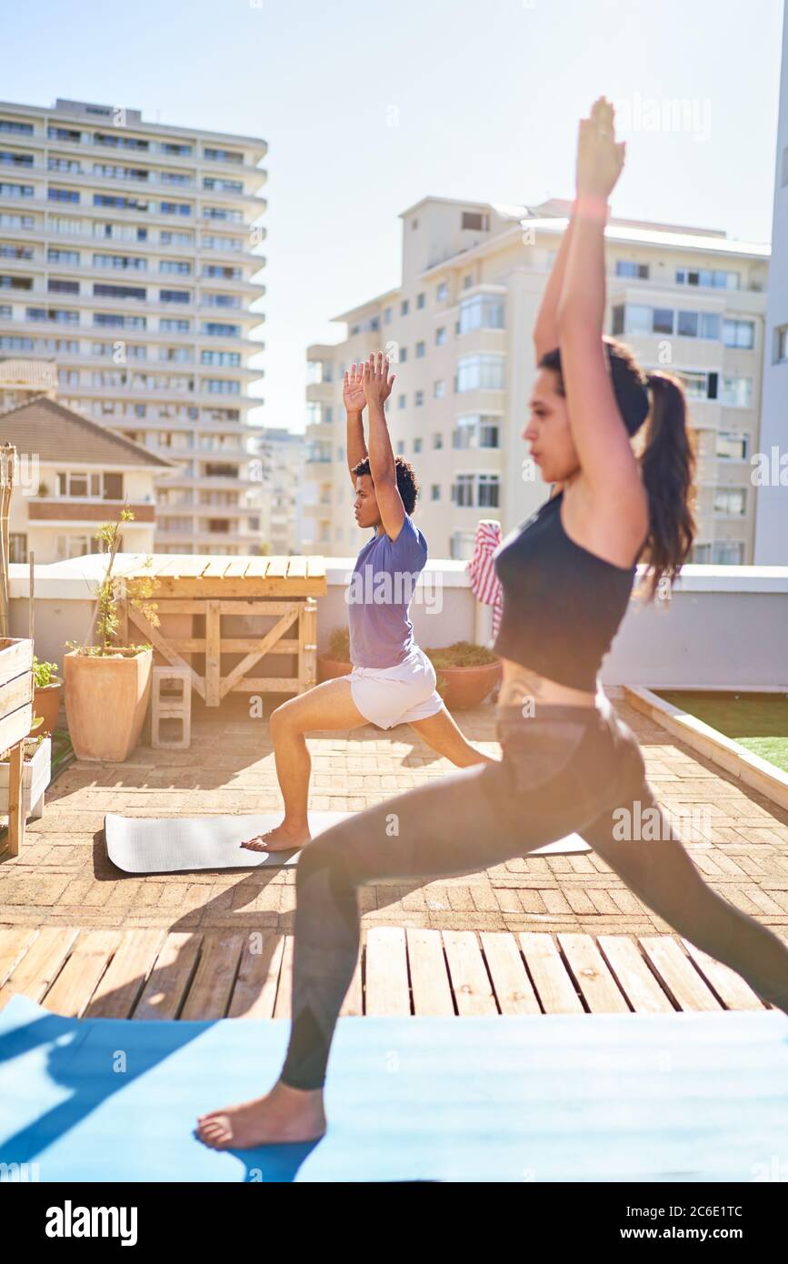 Jeune couple pratiquant le yoga sur le balcon urbain ensoleillé du toit Banque D'Images