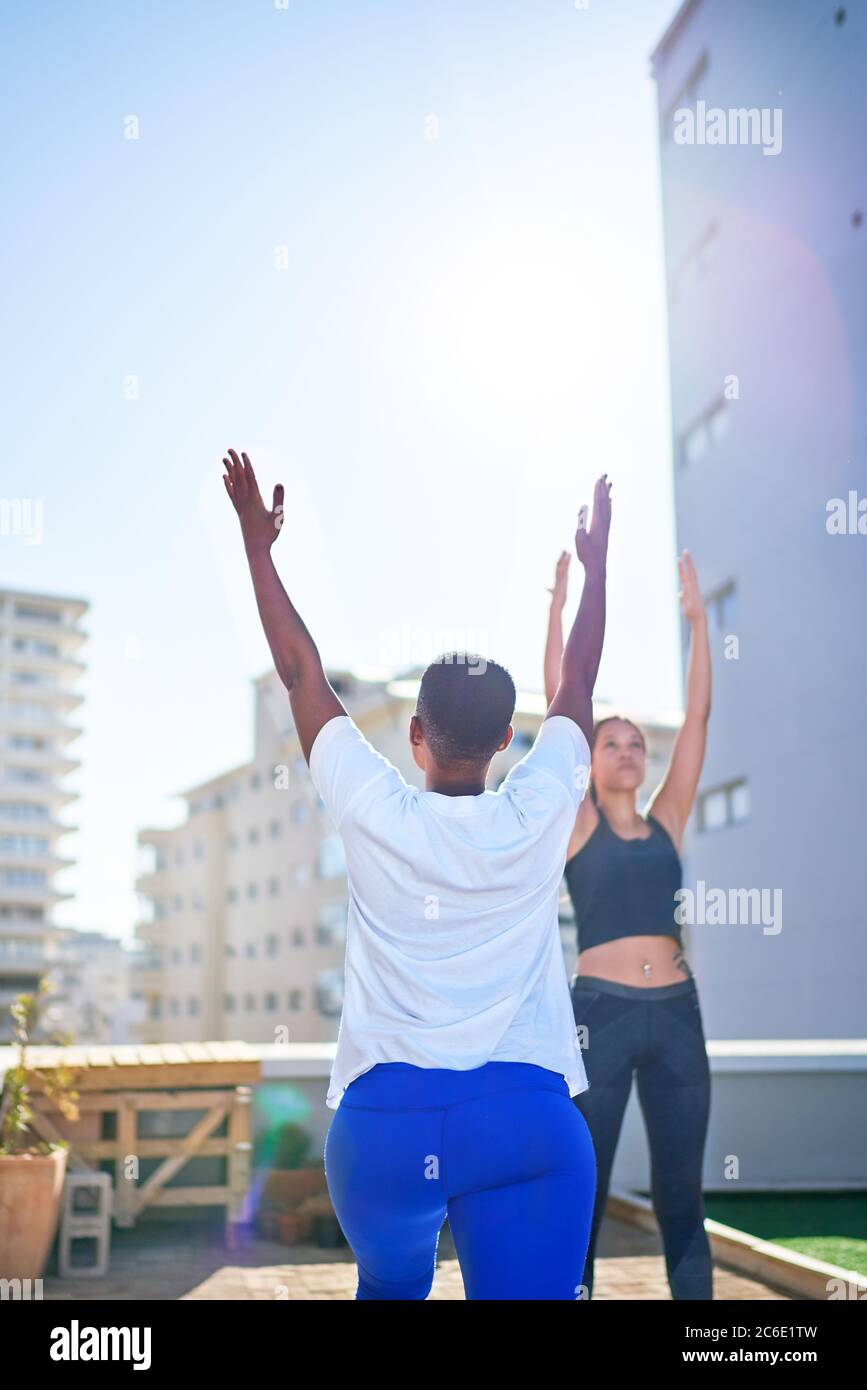 Jeunes femmes pratiquant le yoga sur le balcon urbain ensoleillé sur le toit Banque D'Images