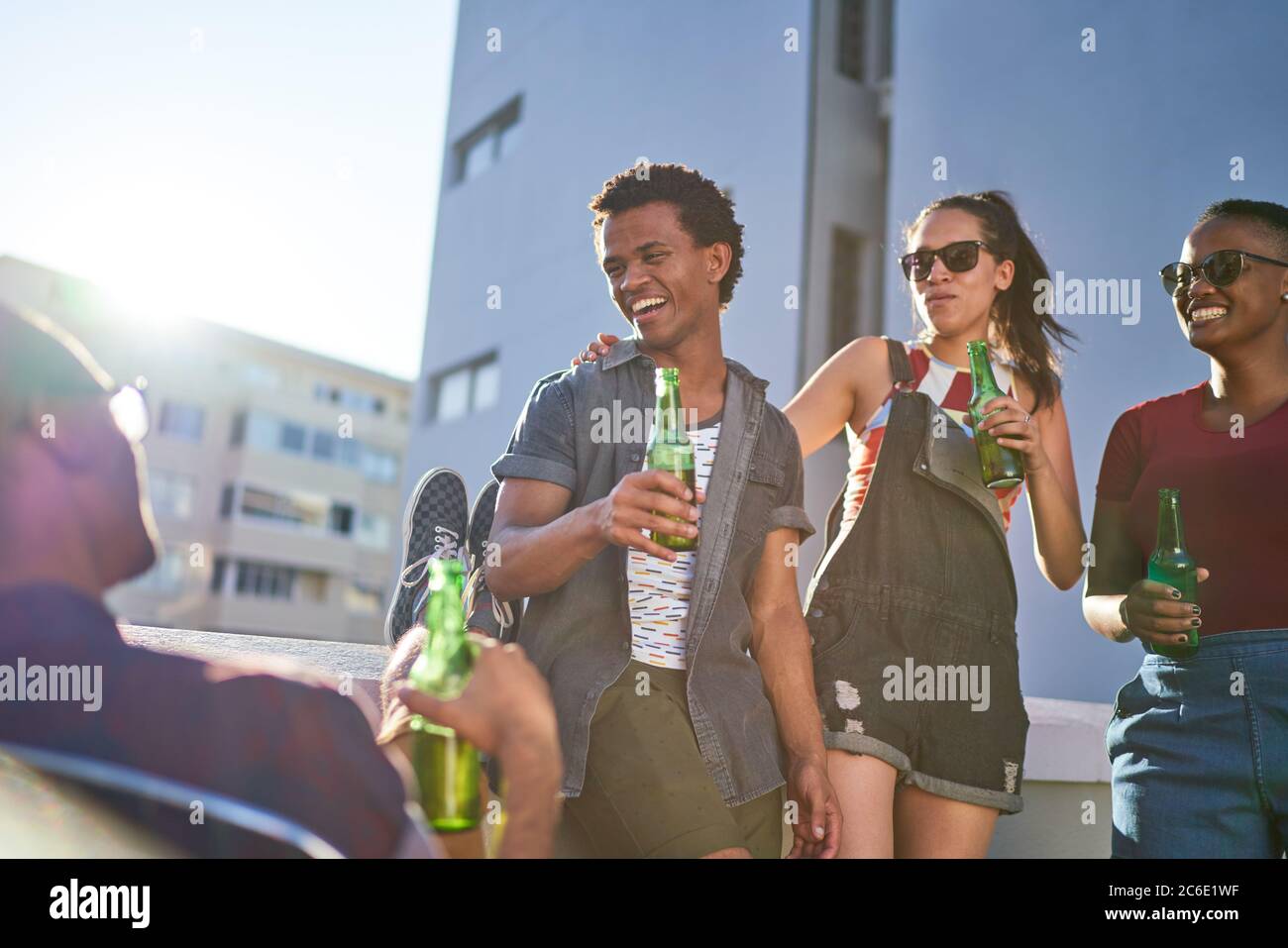 De jeunes amis heureux buvant de la bière sur un balcon urbain ensoleillé Banque D'Images