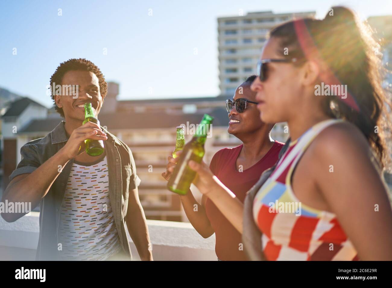De jeunes amis heureux buvant de la bière sur le balcon urbain ensoleillé sur le toit Banque D'Images