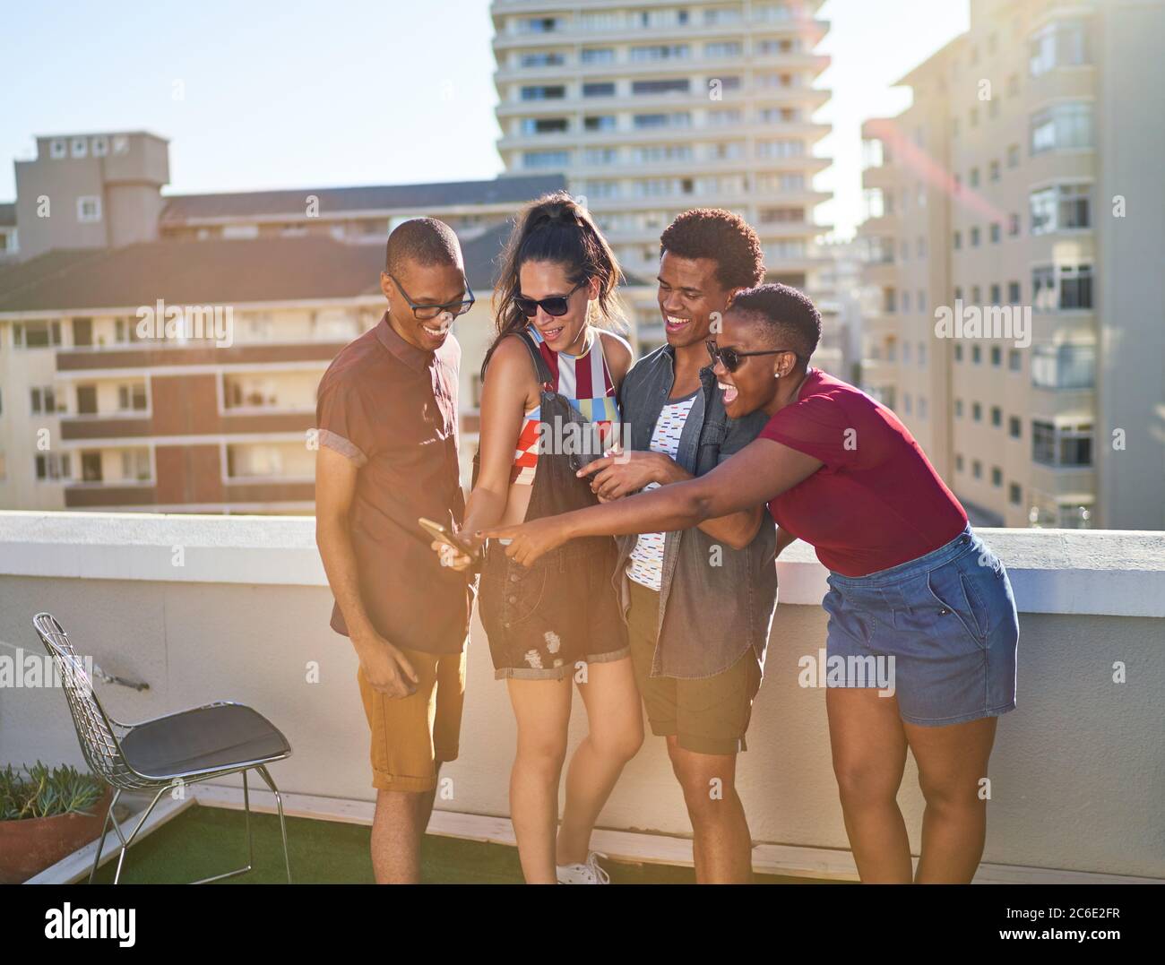De jeunes amis heureux avec un smartphone sur un balcon urbain ensoleillé Banque D'Images