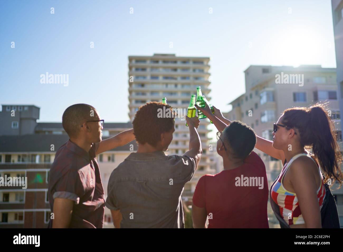 Des jeunes amis toastent des bouteilles de bière sur le balcon urbain ensoleillé sur le toit Banque D'Images