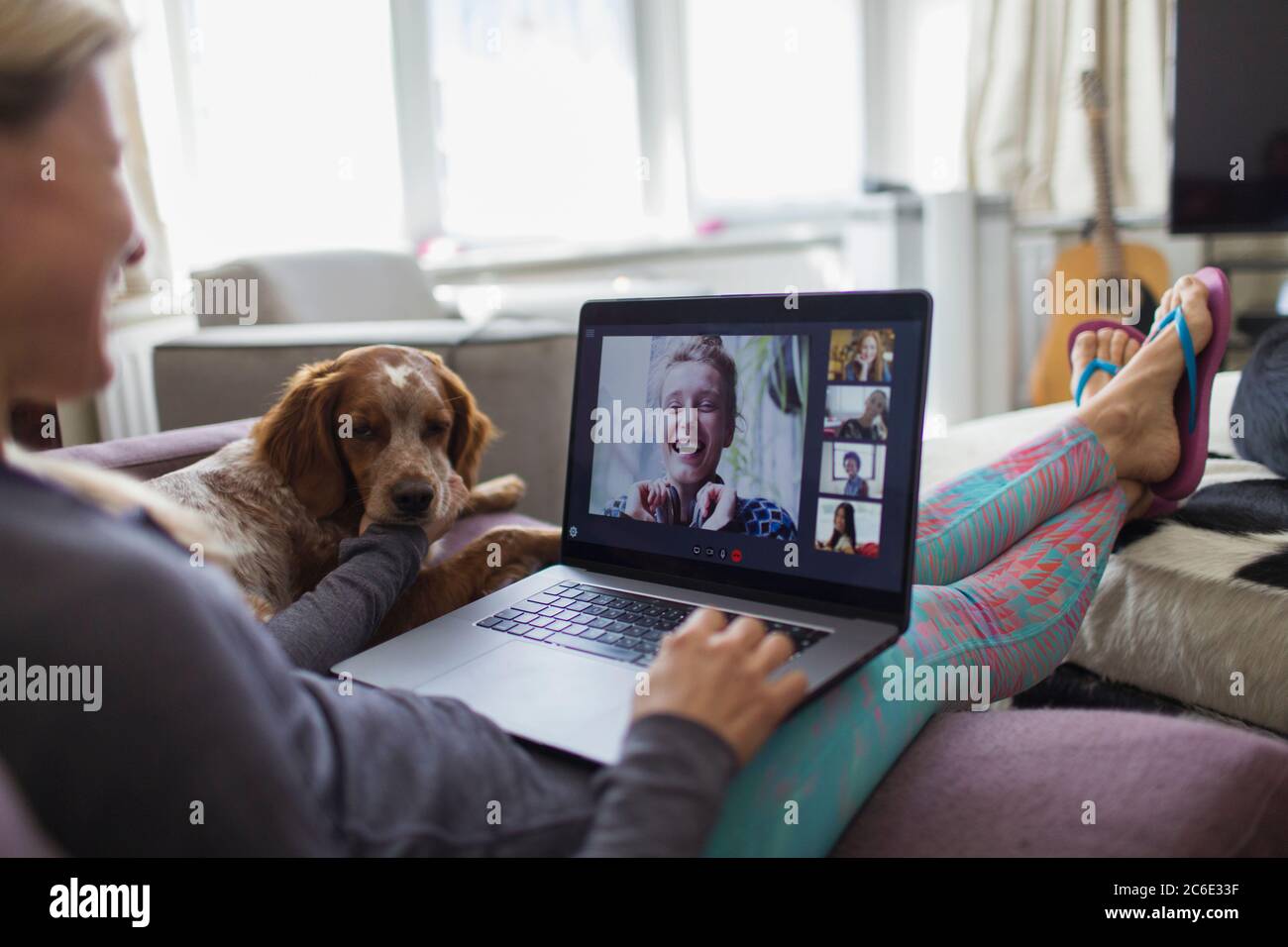 Femme avec un ordinateur portable, discutant vidéo avec des amis sur un canapé avec un chien Banque D'Images