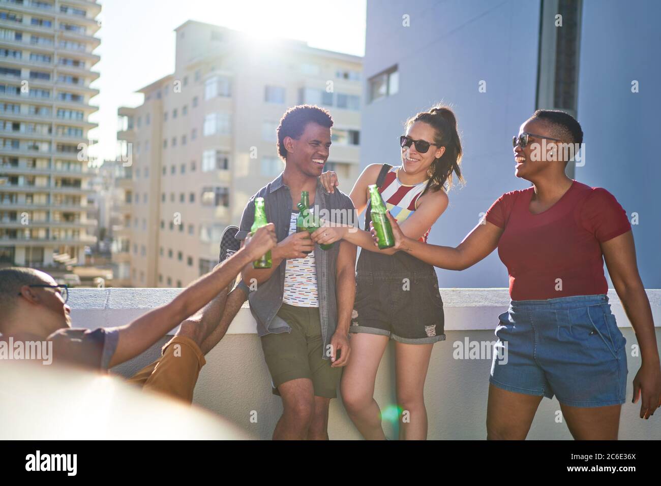 De jeunes amis heureux en dégustant des bouteilles de bière sur un balcon urbain ensoleillé Banque D'Images