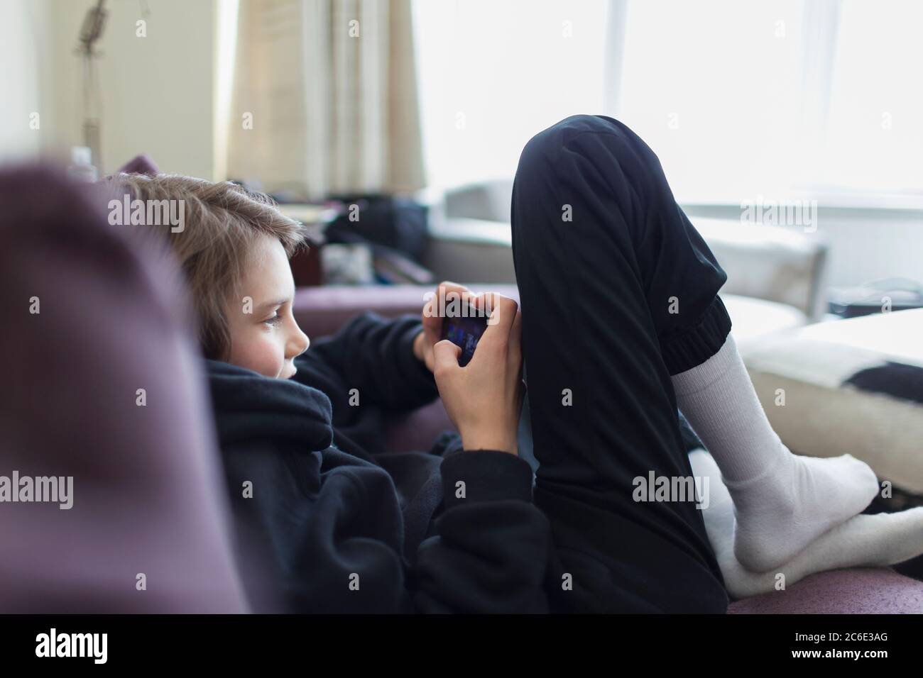 Garçon jouant à un jeu vidéo avec un smartphone sur un canapé Banque D'Images