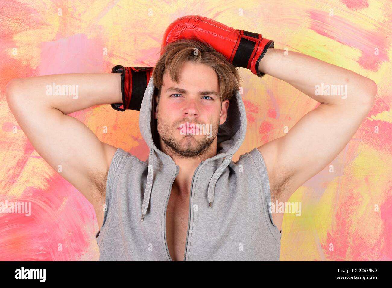 Sports box et combat. Calecon avec visage reflechi tient les mains derriere la tete. Homme avec des cheveux salissants sur fond colore. Guy en gris sans manches porte des gants de boxe