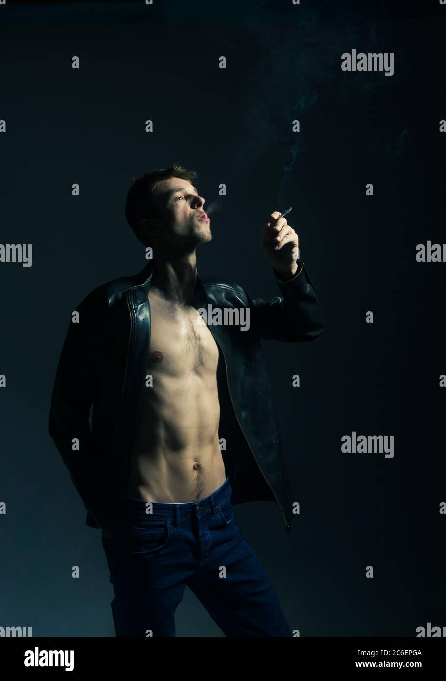 Portrait d'un homme brutal dans une veste en cuir noir. Bascule avec cigarette sur fond noir. Banque D'Images