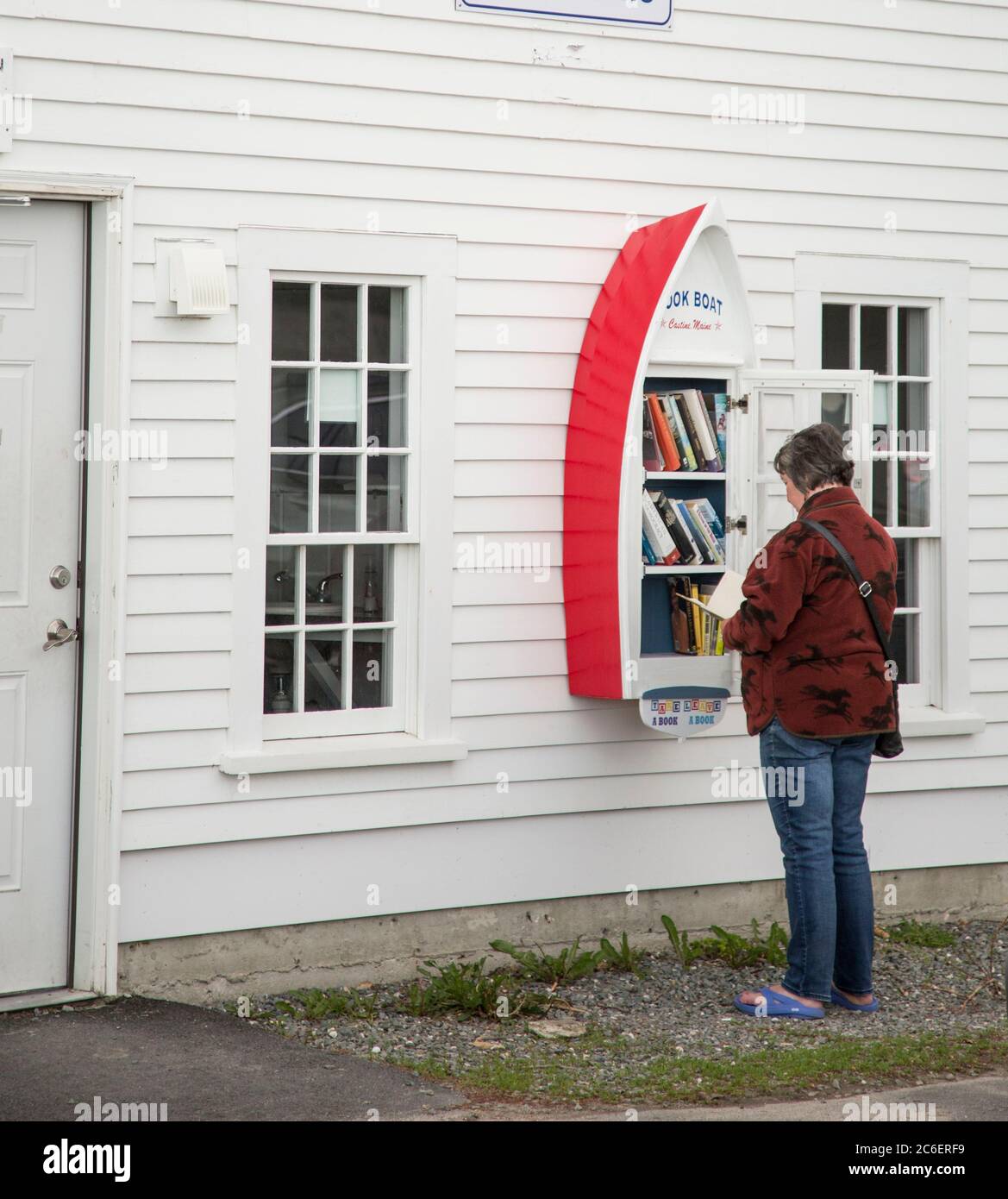 Femme parcourant la petite bibliothèque libre, partage de livres en forme de bateau, Castine, Maine, Etats-Unis Banque D'Images