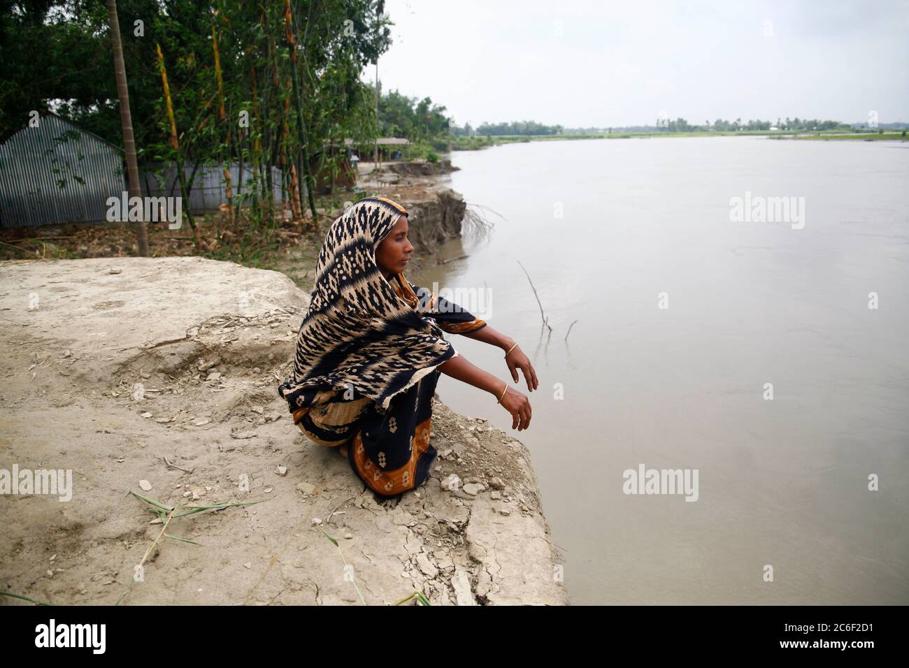 Manikganj. 9 juillet 2020. Une femme est assise sur la rive à côté du site où sa maison a été emmenée le long d'une rivière dans le district de Manikganj, à environ 63 km au nord-ouest de la capitale Dhaka, Bangladesh, le 9 juillet 2020. Les inondations causées par les fortes pluies et la ruée vers l'eau des collines ont gravement affecté les villageois ici. Crédit: Xinhua/Alay Live News Banque D'Images