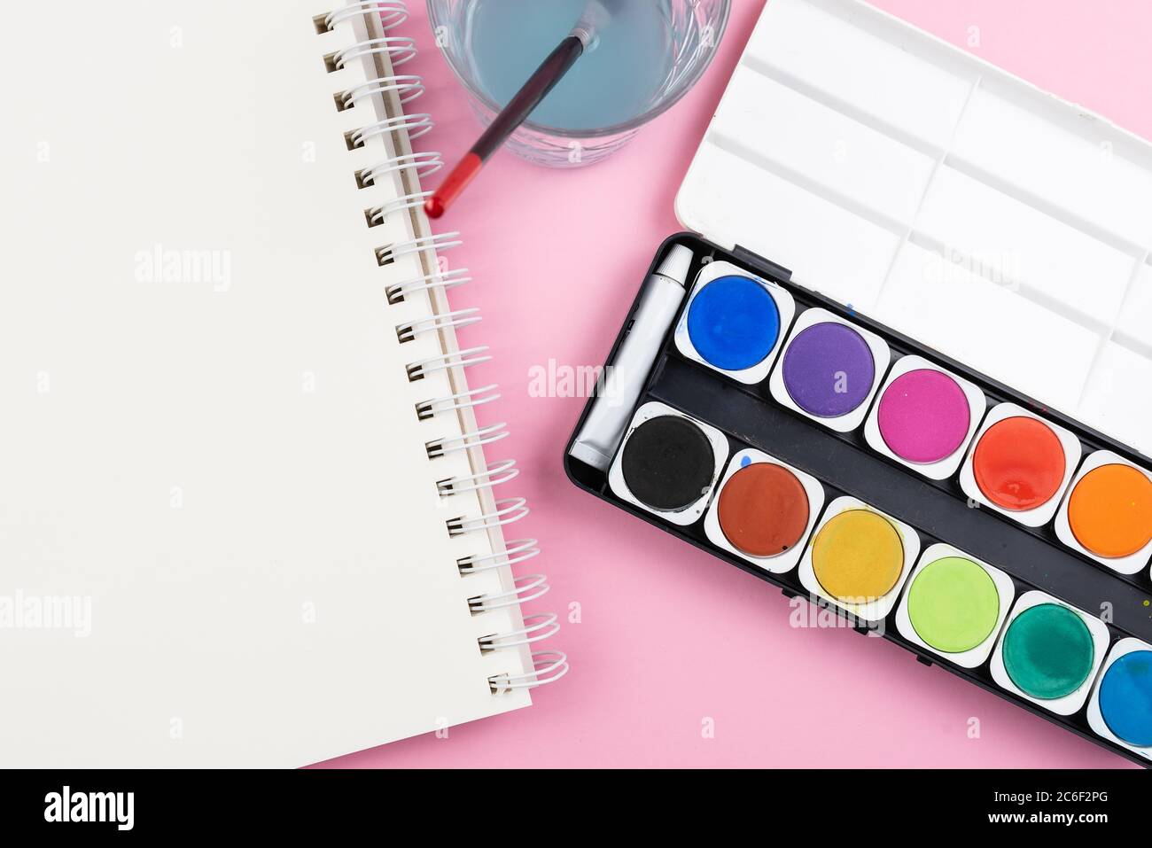 vue au-dessus de la peinture aquarelle, pinceau, carnet d'esquisses et verre d'eau sur fond rose, peinture avec aquarelles et étant un concept créatif Banque D'Images