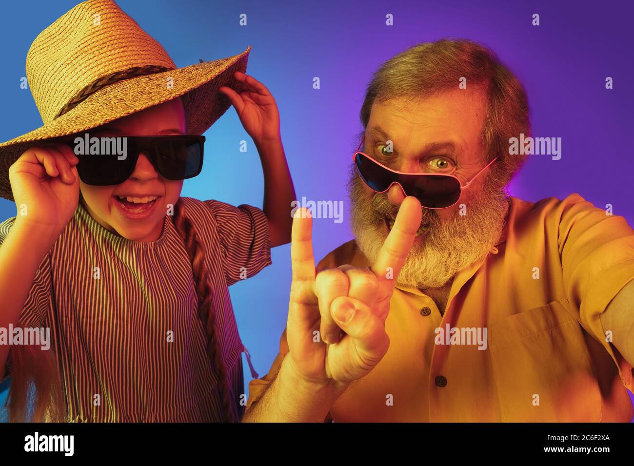 Le retour de la mode rétro. Homme de haut niveau passant du temps heureux avec la petite-fille au néon. Mode de vie joyeux des personnes âgées, famille, enfance, concept technologique. Porter un chapeau et des lunettes de soleil à l'ancienne. CopySpace. Banque D'Images