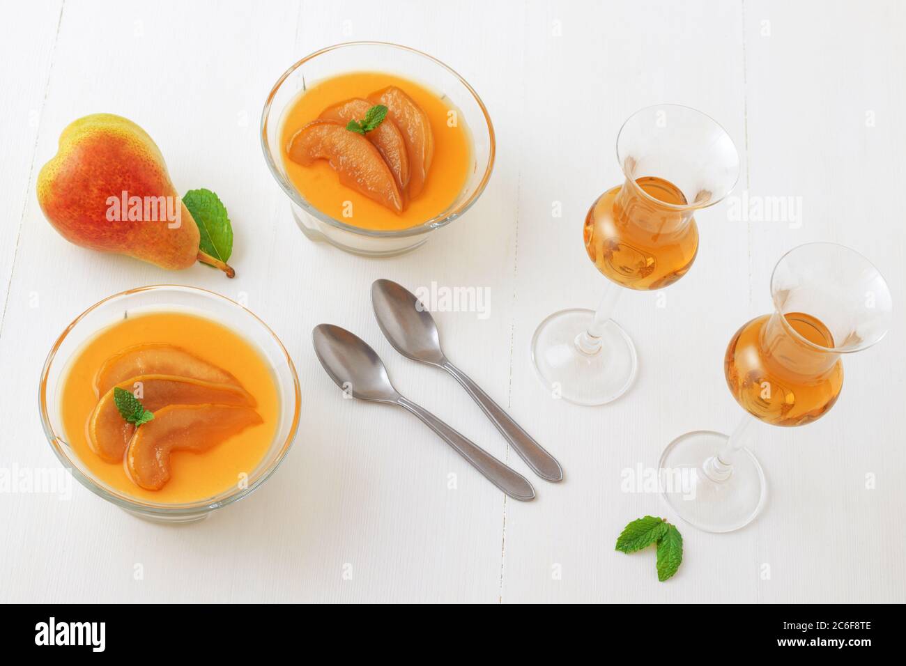 Panna cotta dessert traditionnel italien avec poires pochées dans le rhum et le sirop de miel avec un verre de rhum. Vue en grand angle, le tout sur une table en bois blanc. Banque D'Images
