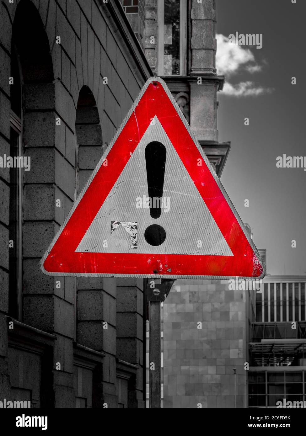 un panneau triangulaire rouge encadré avec un point d'exclamation signale un danger à côté des bâtiments. photographie en noir et blanc Banque D'Images