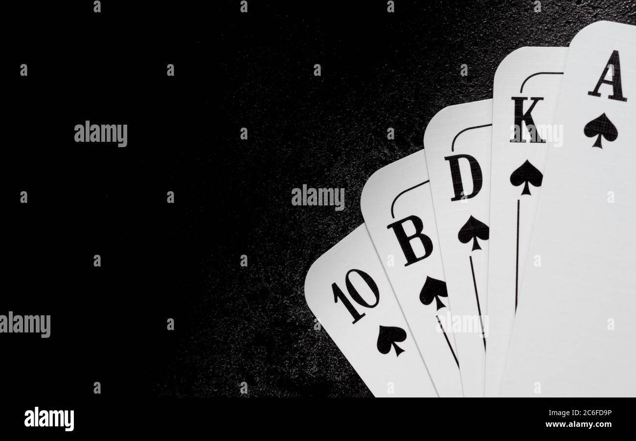 cinq cartes à jouer blanches de spades formant une quinte royale dans le coin inférieur droit sur une surface en fonte noire avec un espace de copie sur le côté gauche Banque D'Images