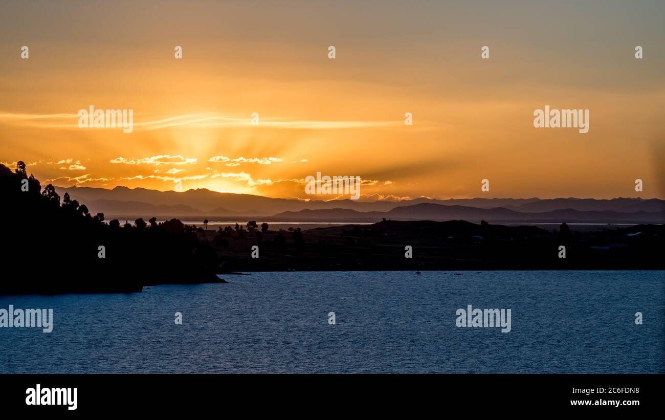 coucher de soleil avec un ciel nuageux orange et la formation de rayons de soleil sur le lac titicaca, l'eau en premier plan avec un paysage étendu et le brouillard dans la vallée Banque D'Images
