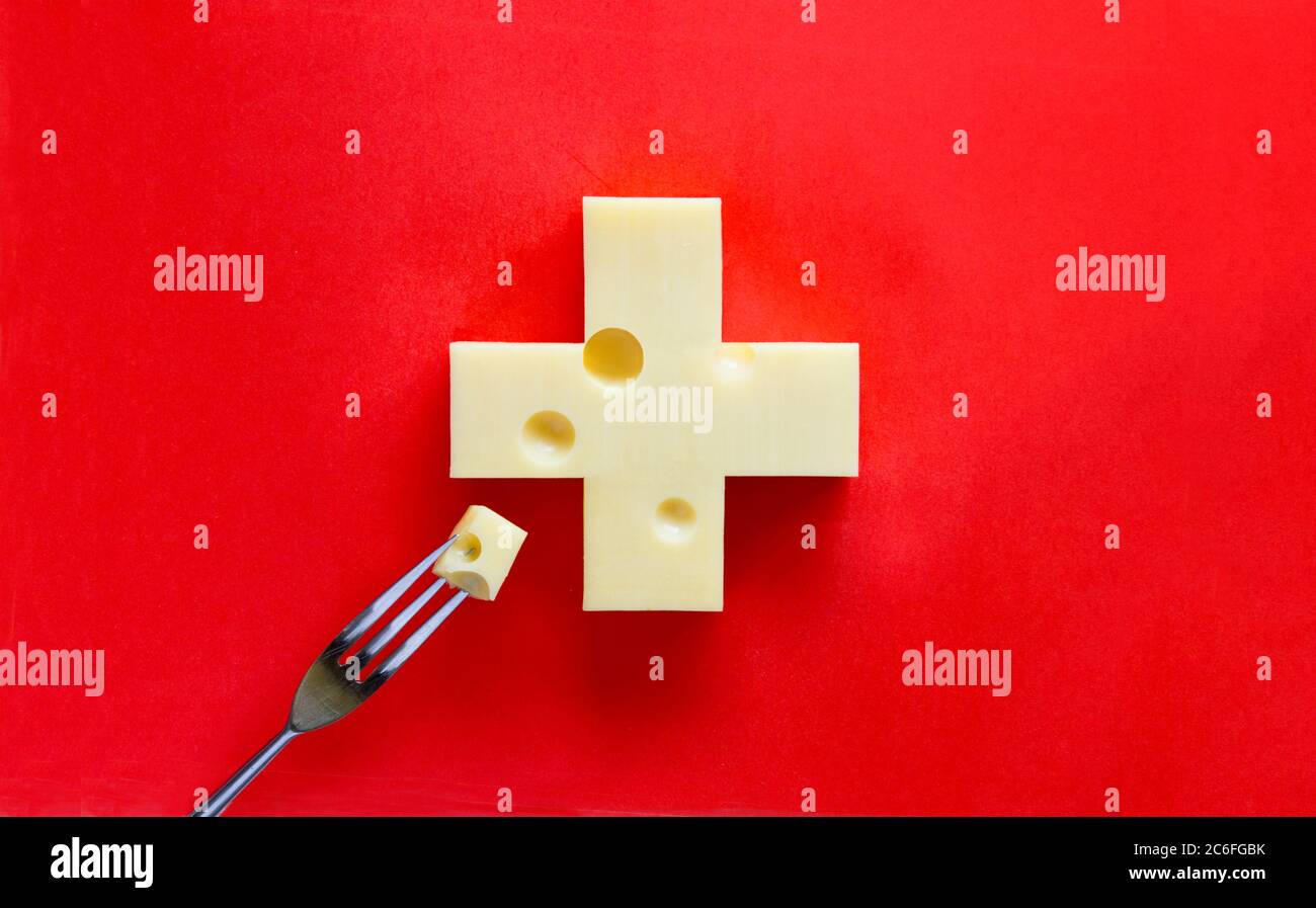 Croix suisse sous forme de fromage sur fond rouge, avec un morceau sur la fourchette Banque D'Images