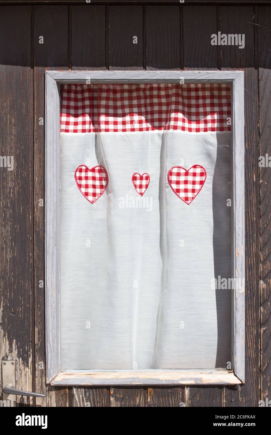 Rideau de fenêtre aux formes coeur rouge sur une maison de chalet en bois dans la région des Alpes Banque D'Images