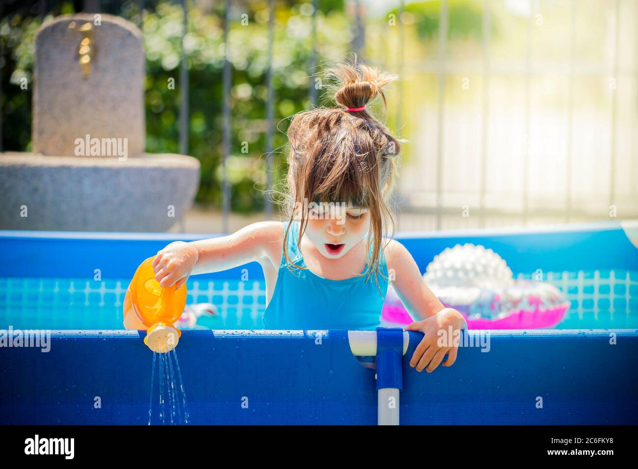 Petite fille caucasienne, dans une piscine bleue, jouant avec un jouet arrosoir peut un jour d'été brillant. Effet du réchauffement climatique ou de la température chaude Banque D'Images