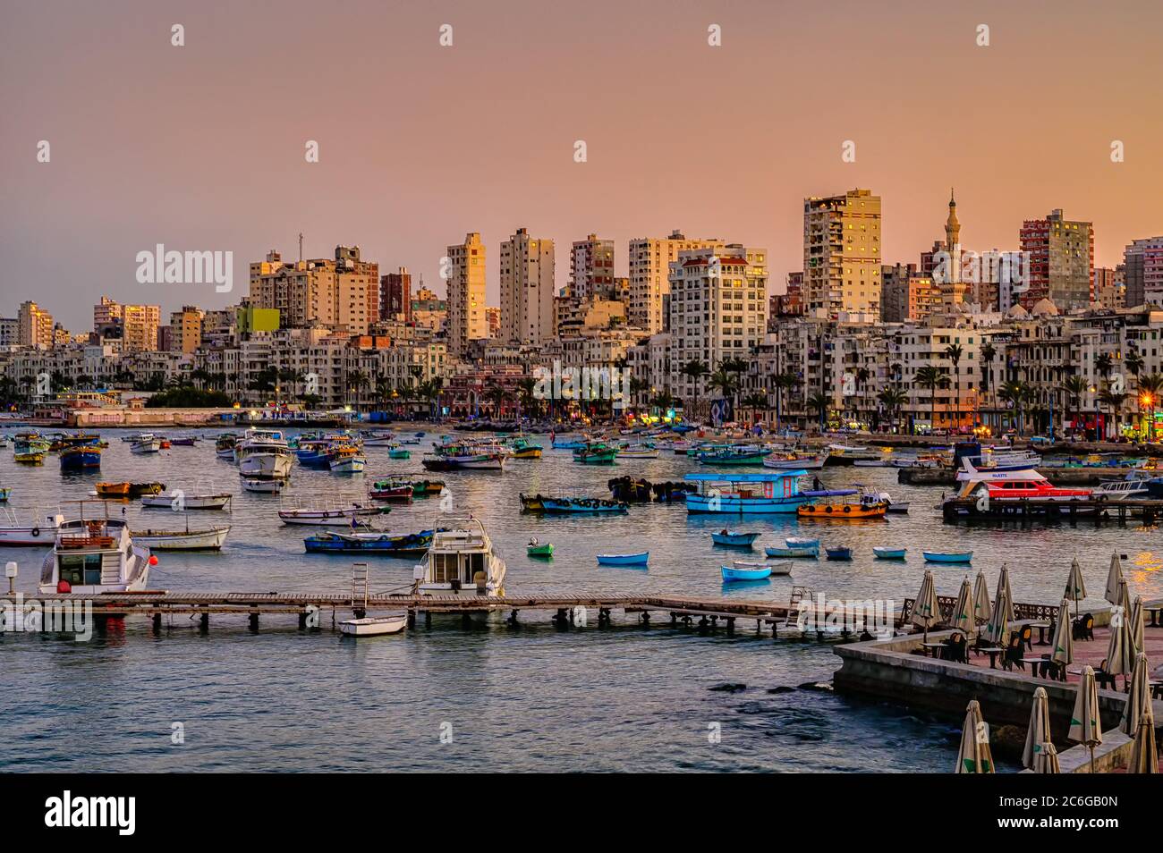 Soleil couchant sur la flotte de pêche du port oriental et la skyline du centre-ville d'Alexandrie en Égypte Banque D'Images