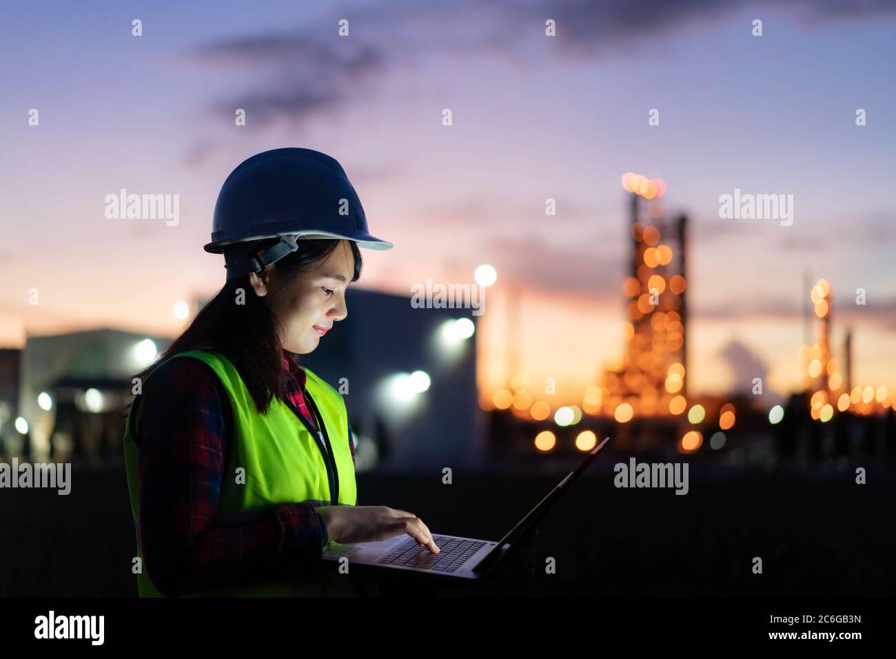 Femme asiatique ingénieur pétrochimique travaillant la nuit avec un ordinateur portable dans l'usine de raffinage de pétrole et de gaz la nuit pour la sécurité des inspecteurs Banque D'Images
